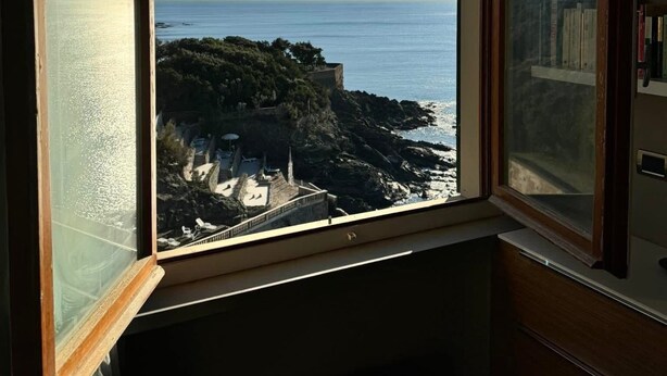 Ein Zimmer mit großem Fenster mit Blick auf eine zerklüftete Küste und das Meer.