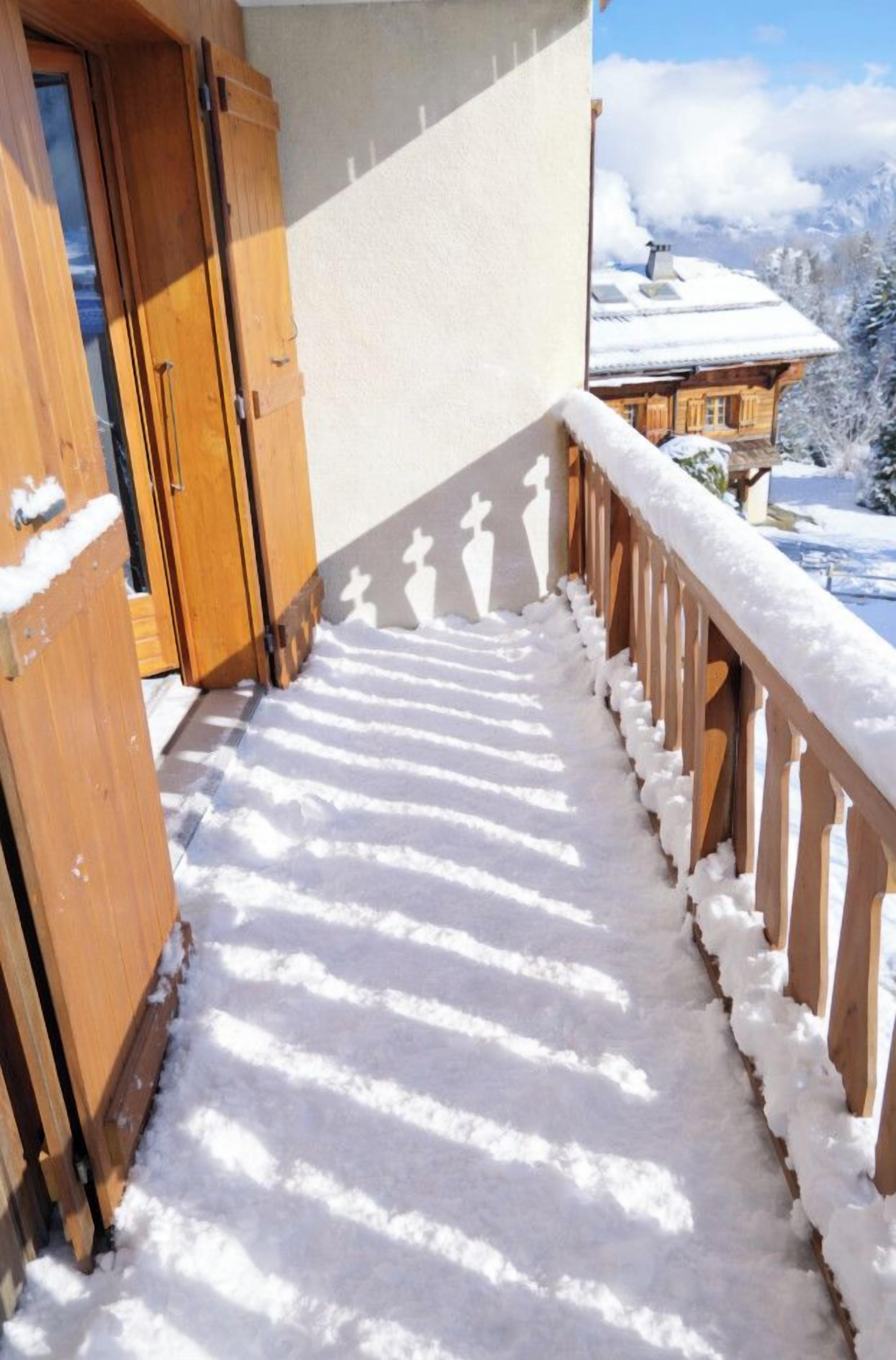 A snow-covered balcony with wooden railings and a wooden door.