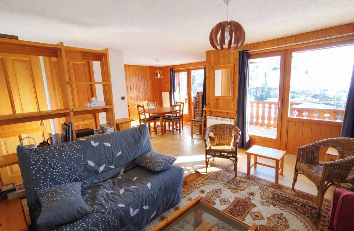 A cozy living room with a sofa, chairs, a dining table, and a balcony with wooden railings.