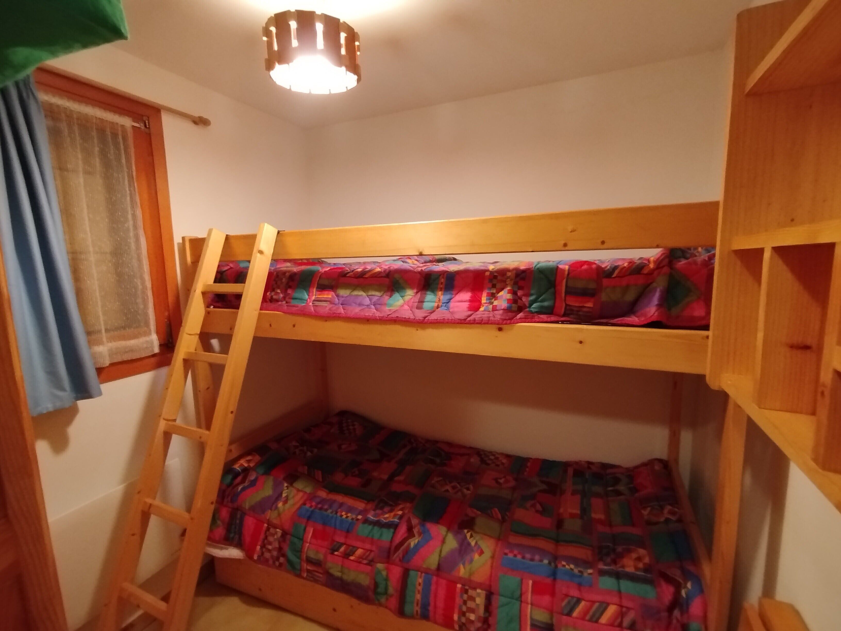 Un letto a castello con una scaletta, una coperta colorata e una finestra con tende.