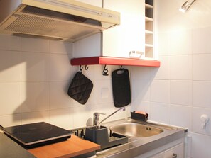 Et køkken med en integreret induktionskogeplade, en stålvask og en rød hylde over bordpladen.