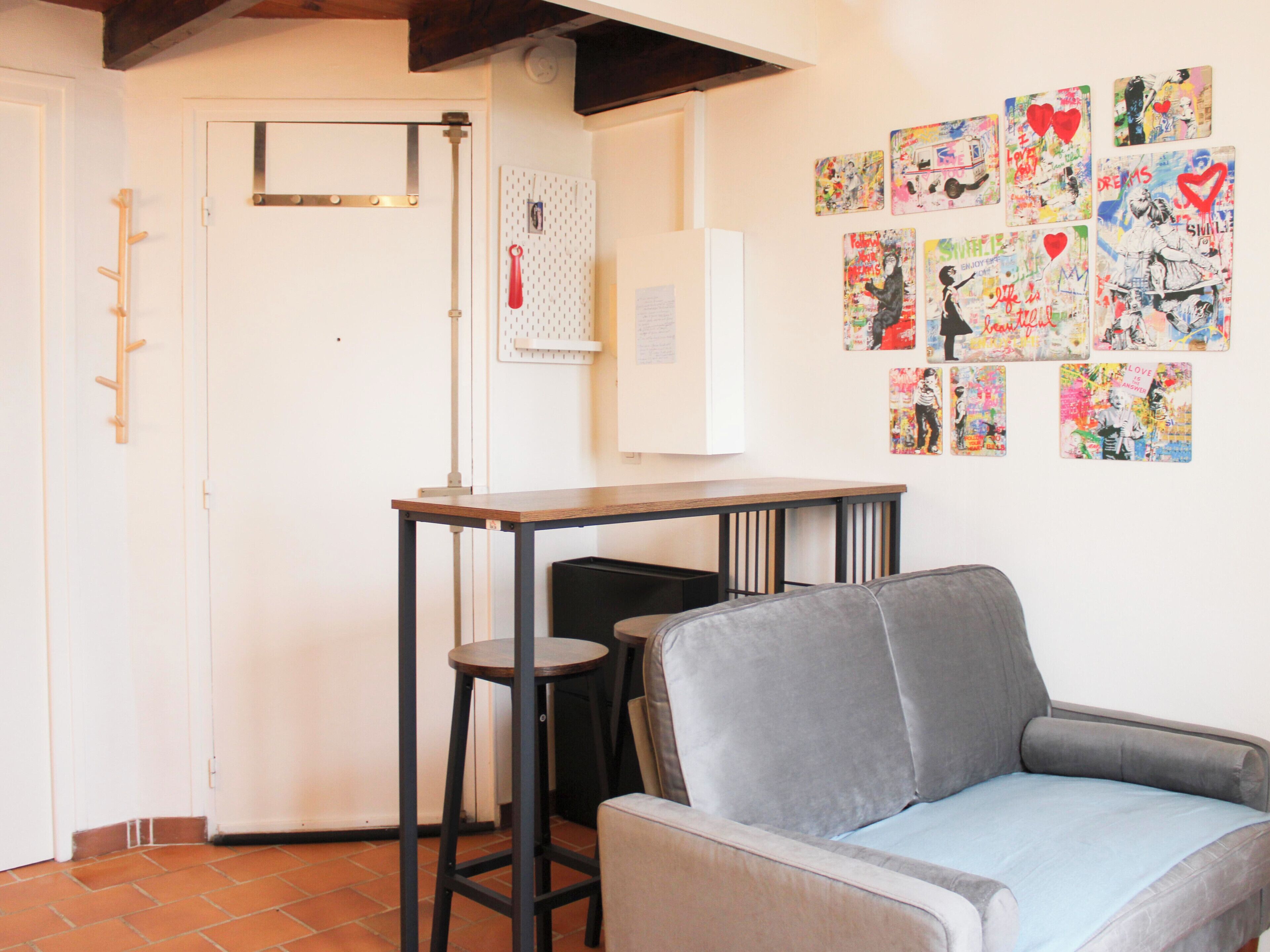 A room with a grey sofa, a small table, and a wall adorned with colorful artwork.