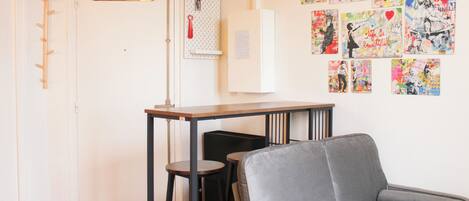 Une pièce avec un canapé gris, une petite table et un mur décoré d’œuvres d’art colorées.