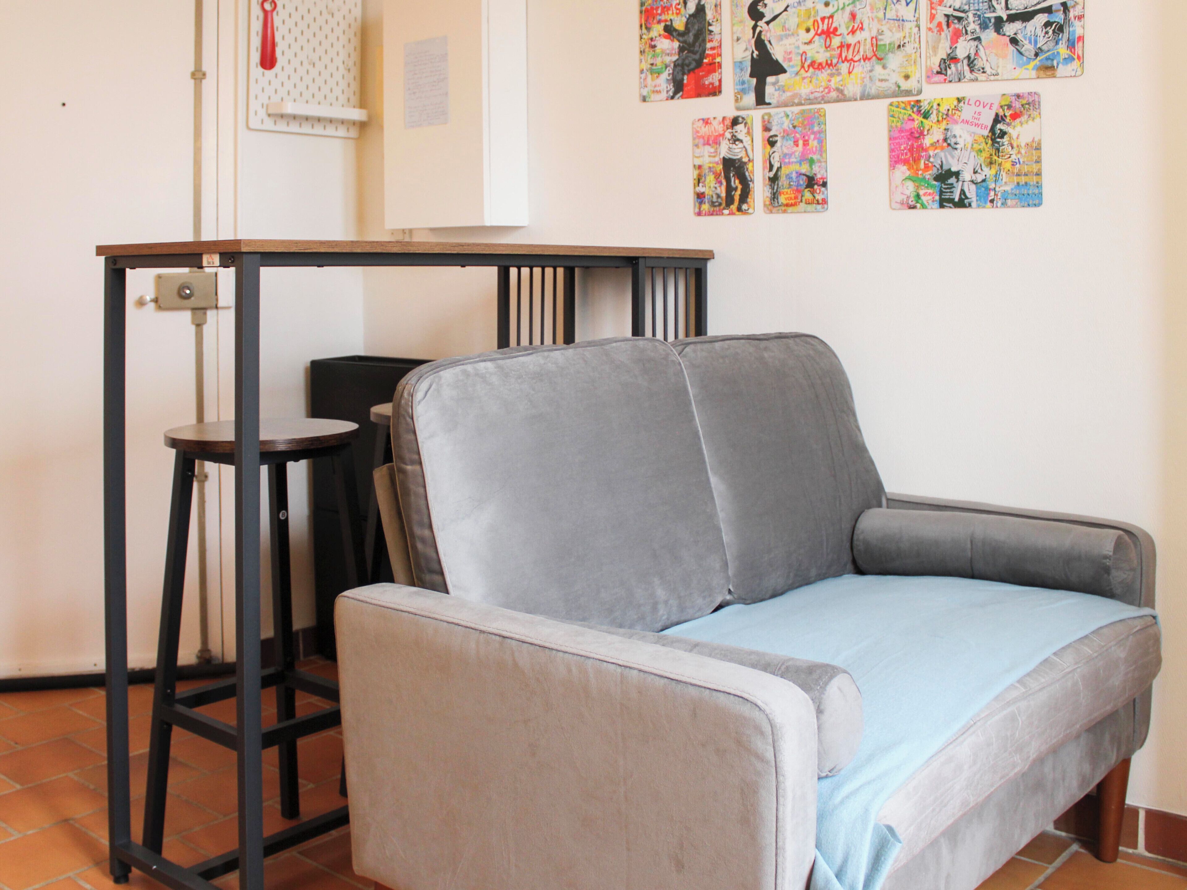 A room with a grey sofa, a small table, and a chair. There are wall decorations and a door with a handle.