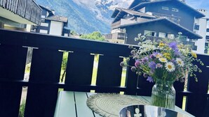 Een balkon met uitzicht op besneeuwde bergen, een vaas met bloemen en een tafel.