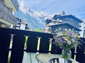 A balcony with a view of snow-capped mountains, a vase with flowers, and a table. - Renovated flat with Mont Blanc's view | Parking (Chamonix-Mont-Blanc)