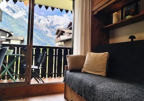 A balcony with a view of snow-capped mountains, a wooden floor, a sofa with cushions, and a chair. - Renovated flat with Mont Blanc's view | Parking (Chamonix-Mont-Blanc)