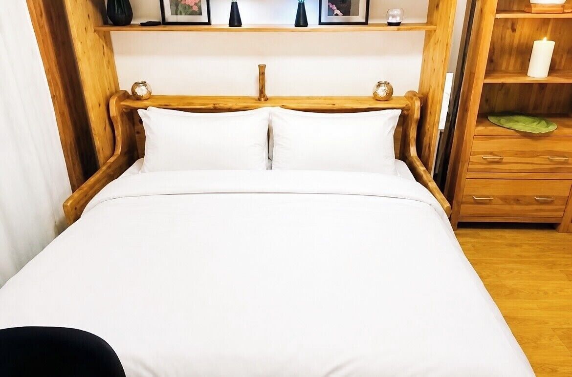 A wooden bed with white bedding, a wooden headboard, and a bedside table with a green cloth.