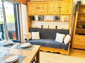 A cozy room with a grey sofa, wooden cabinets, and a dining area with a table set for two. - Renovated flat with Mont Blanc's view | Parking (Chamonix-Mont-Blanc)