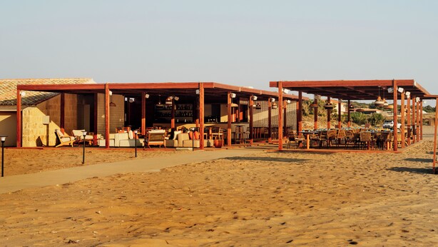 A beachside restaurant with outdoor seating and a bar area. -  Icona's Costa Ragusa Resort - New Opening (Scoglitti)