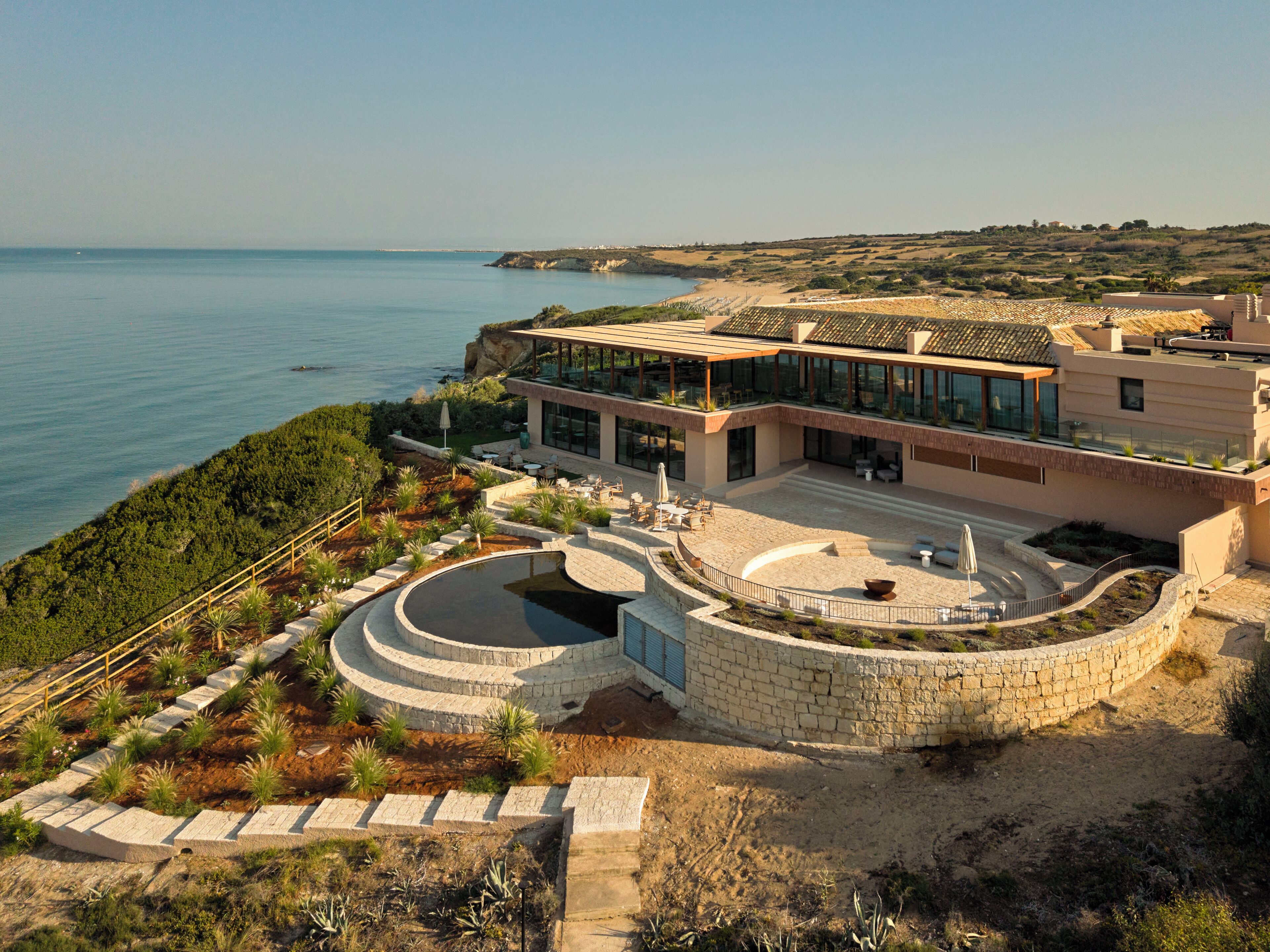 Una moderna proprietà costiera con una grande piscina esterna, un patio e vista sul mare.