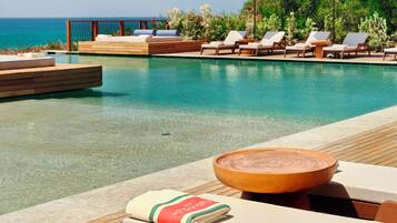 Un espace aménagé au bord de la piscine, avec des chaises longues et des parasols, une terrasse en bois et une vue sur l’océan.