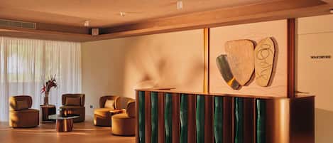 Una moderna zona de recepción con un mostrador de madera, asientos cómodos y un amplio ventanal con cortinas traslúcidas.