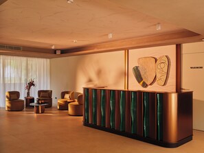 Un espace d’accueil moderne, doté d’un comptoir de réception en bois, de sièges confortables et d’une grande fenêtre agrémentée de rideaux légers.