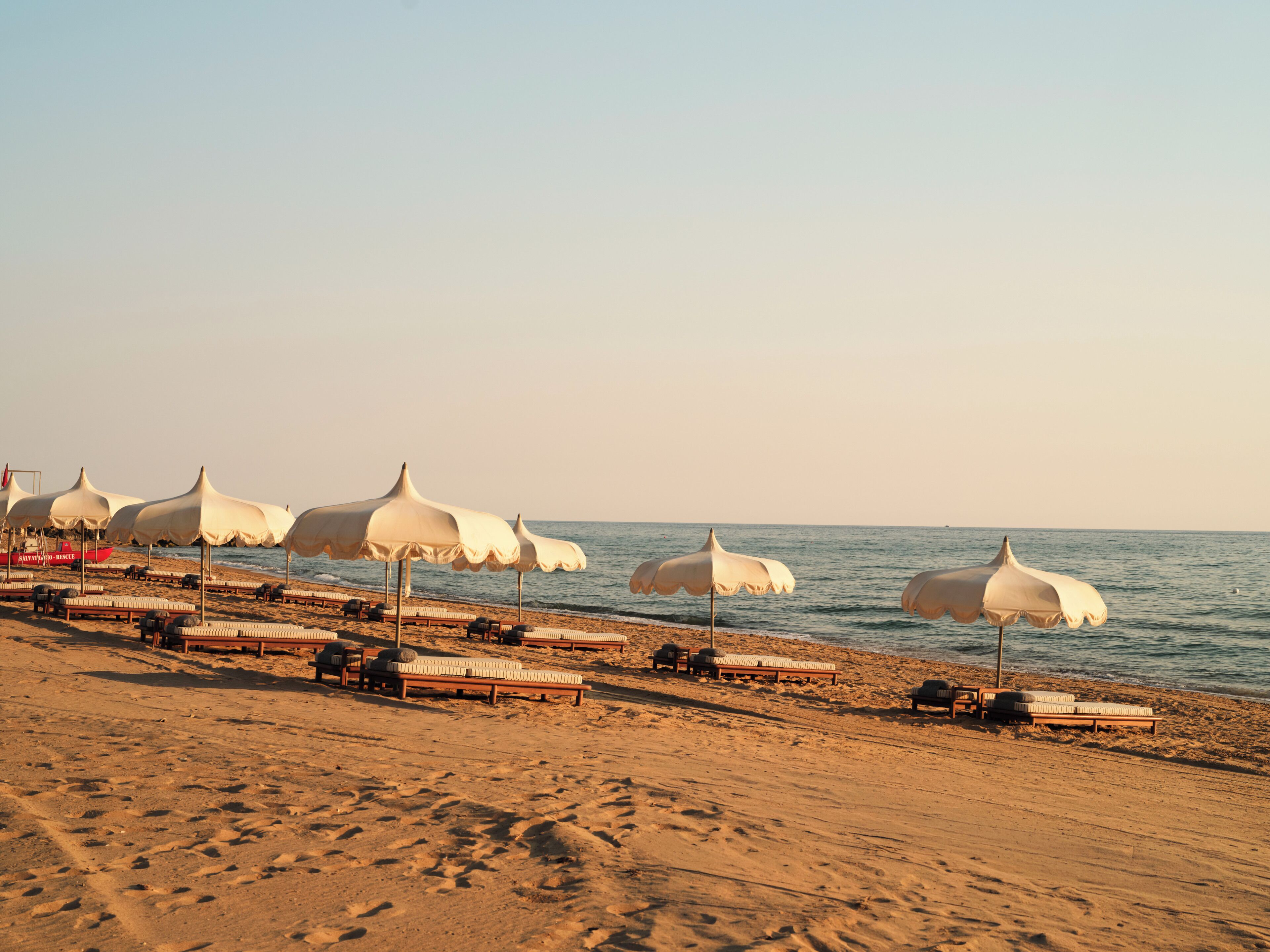 A beach with rows of white umbrellas and wooden lounge chairs.