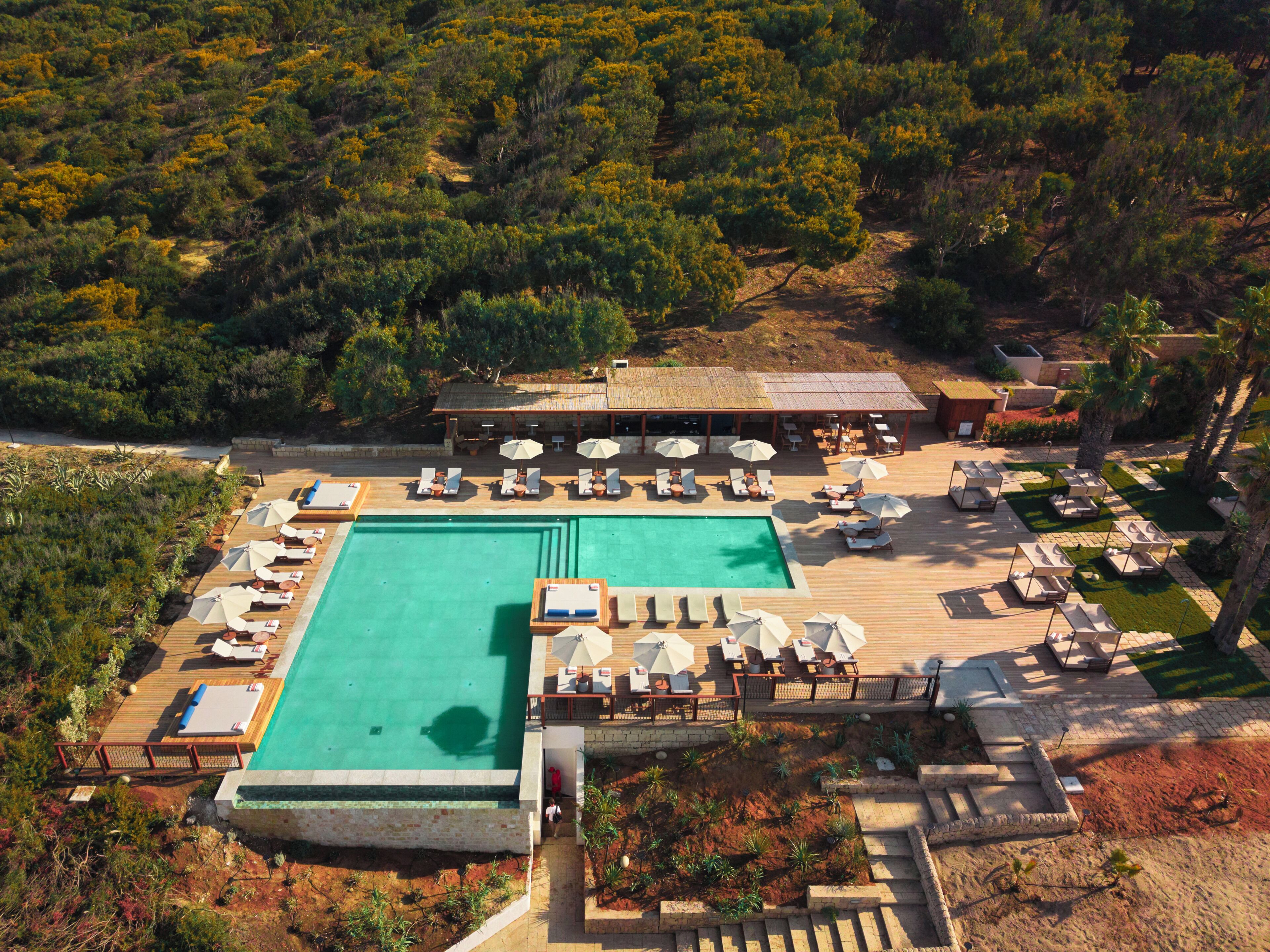 A resort with a large swimming pool, sun loungers, and a covered seating area.