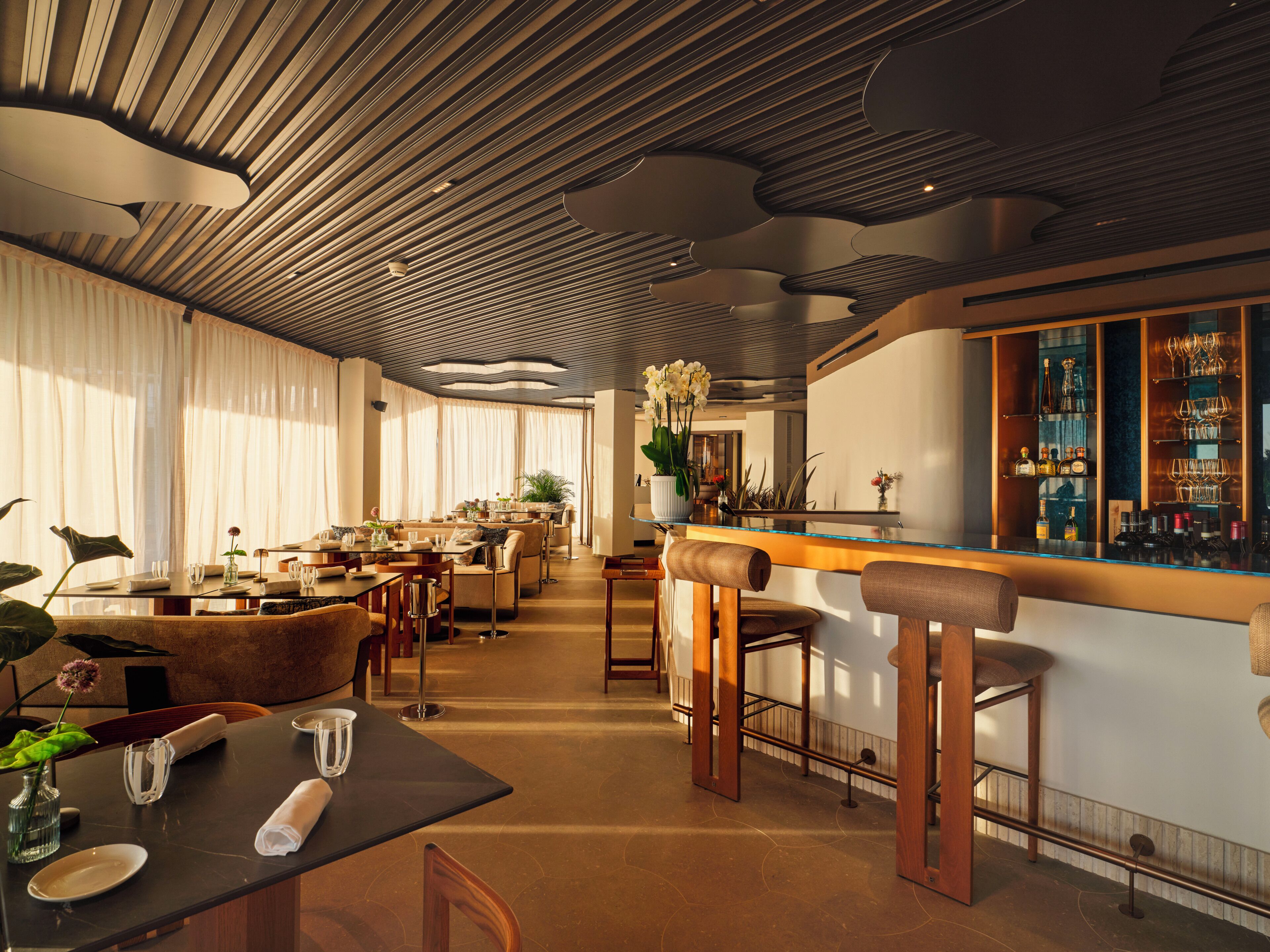 Un restaurante moderno con zona de bar, mobiliario de madera y un techo de diseño único.