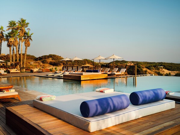 Un espace aménagé au bord de la piscine, avec des chaises longues et des parasols, entouré de palmiers et offrant une vue sur le paysage.
