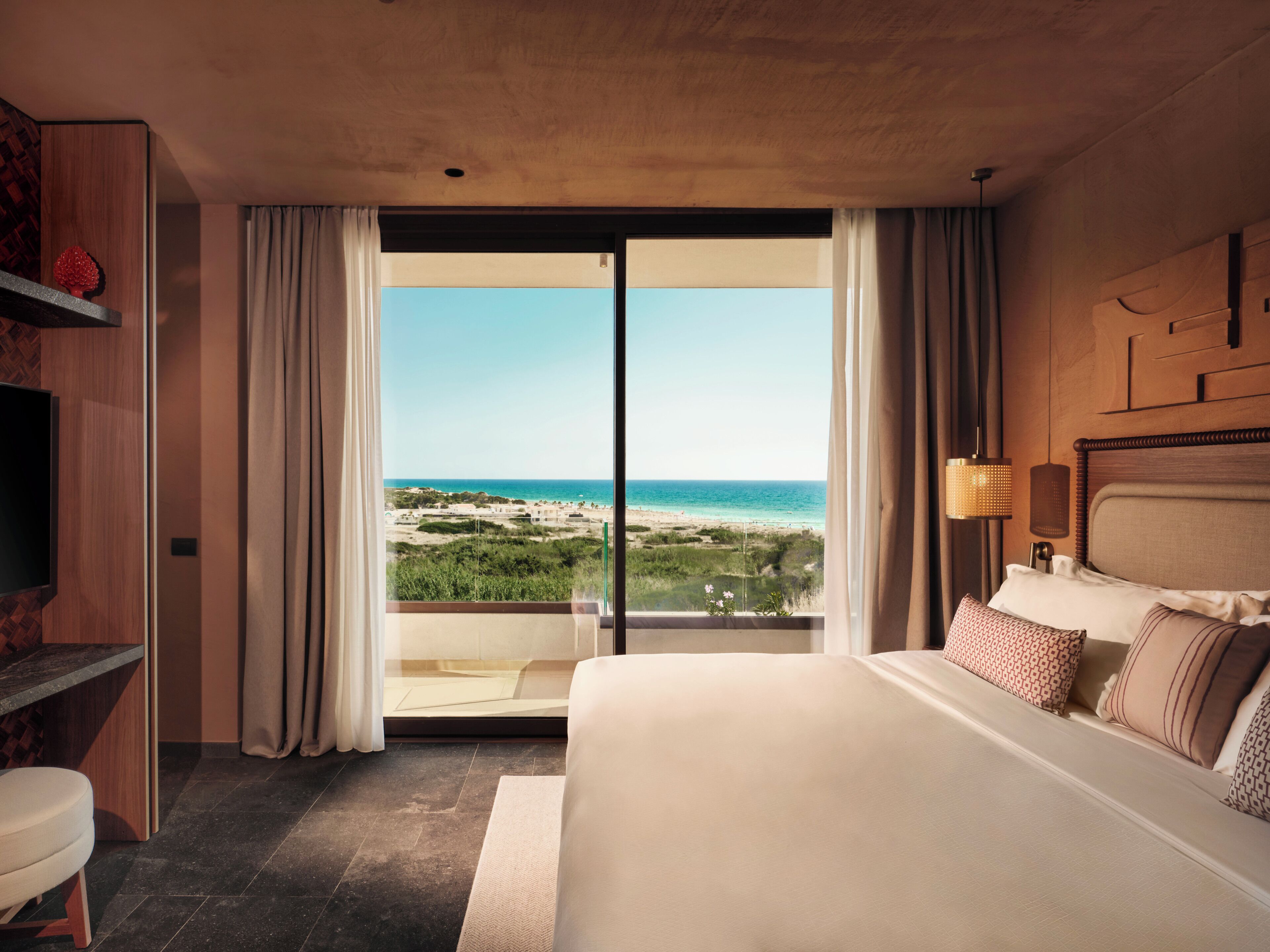 Una camera d'albergo con un letto grande, TV, scrivania e vista sulla spiaggia.
