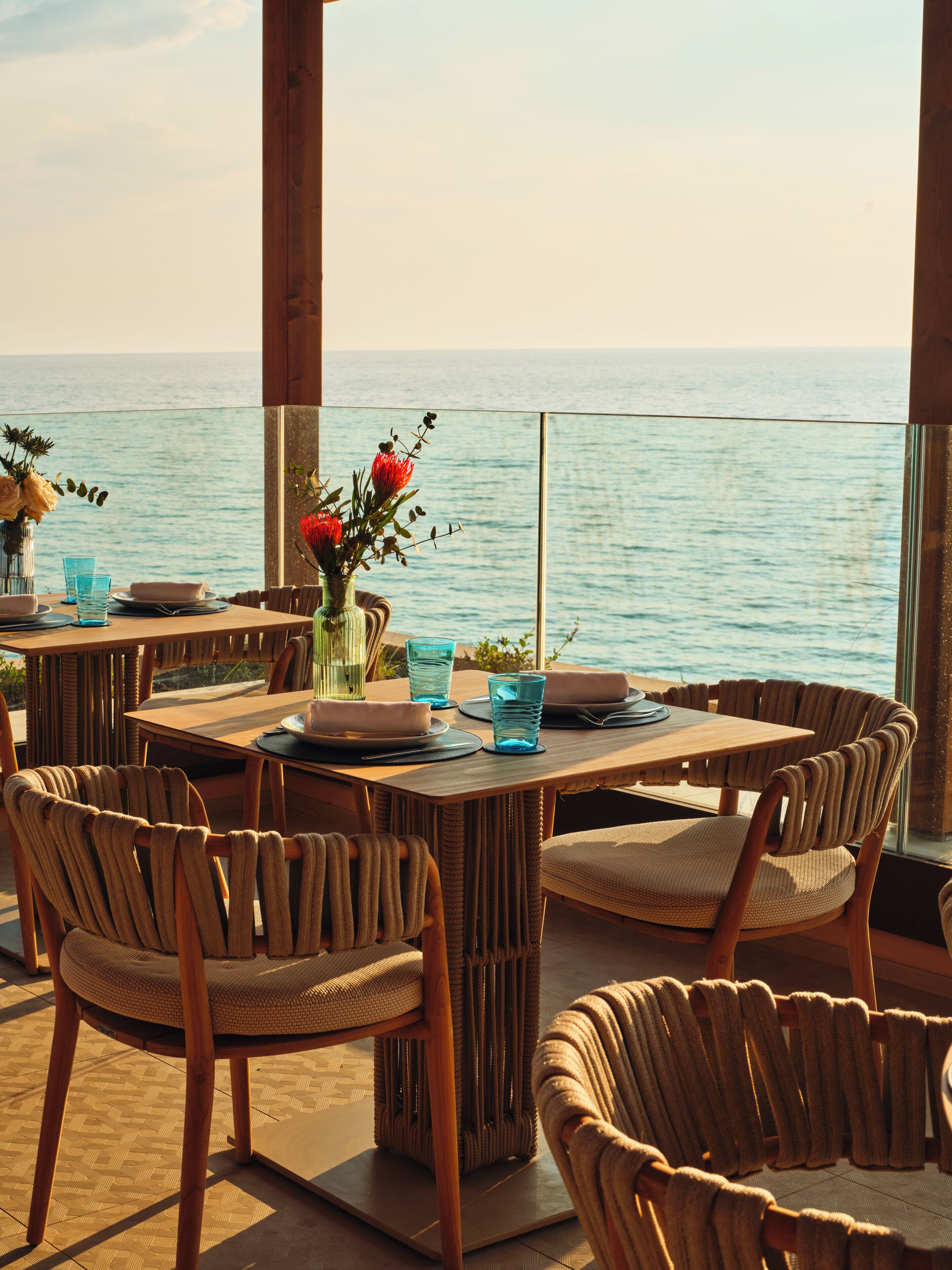 Un espace extérieur aménagé pour les repas, avec des chaises en osier et une table dressée pour deux personnes, offrant une vue sur la mer.