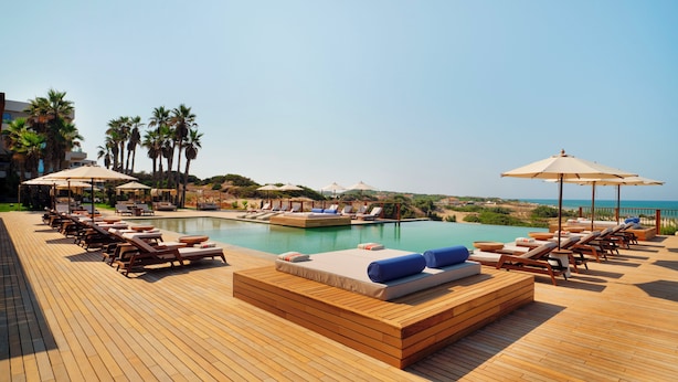 Un espace aménagé au bord de la piscine, avec des chaises longues, des parasols et une terrasse en bois.