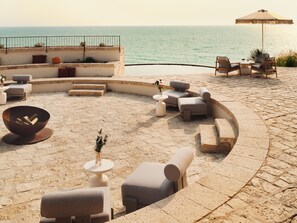 A sunlit outdoor seating area with stone flooring, a round table, and lounge chairs. -  Icona's Costa Ragusa Resort (Scoglitti)