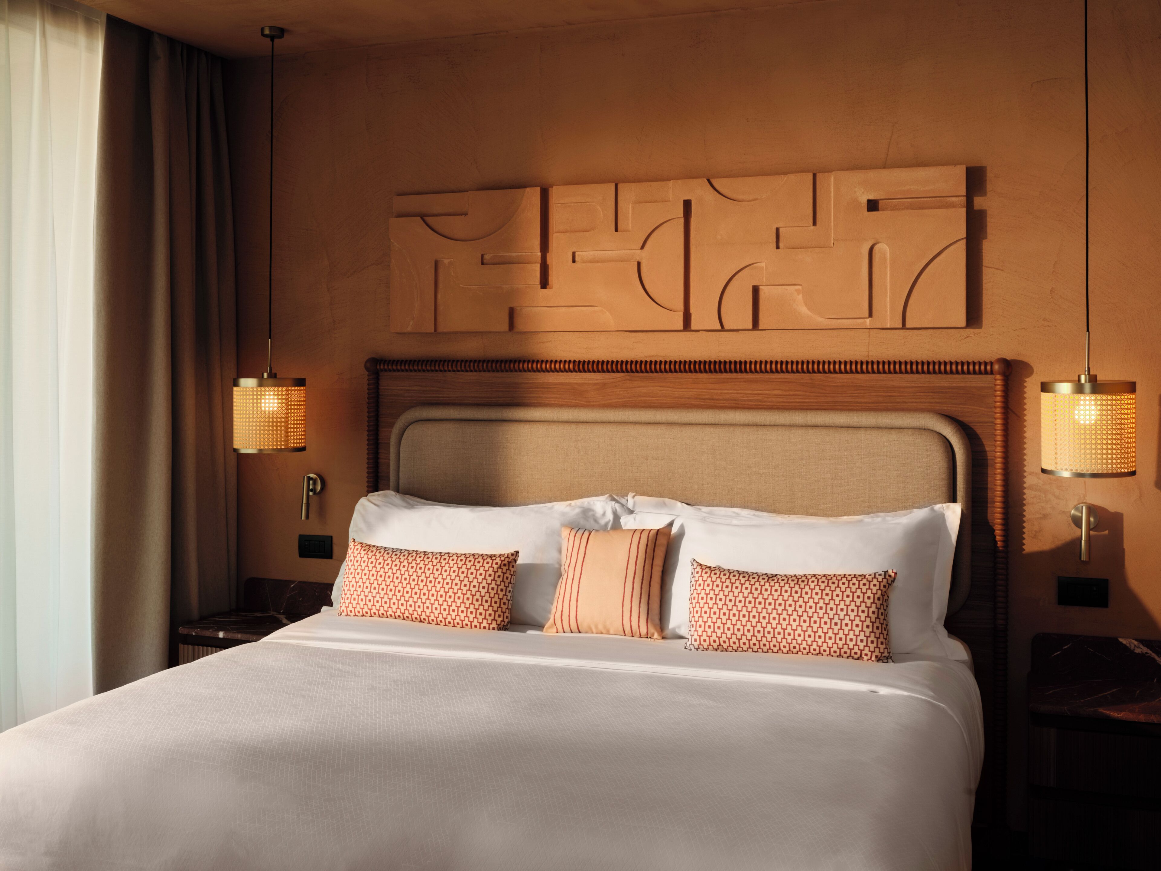 A hotel room with a large bed, two bedside lamps, and a decorative wall panel above the bed.