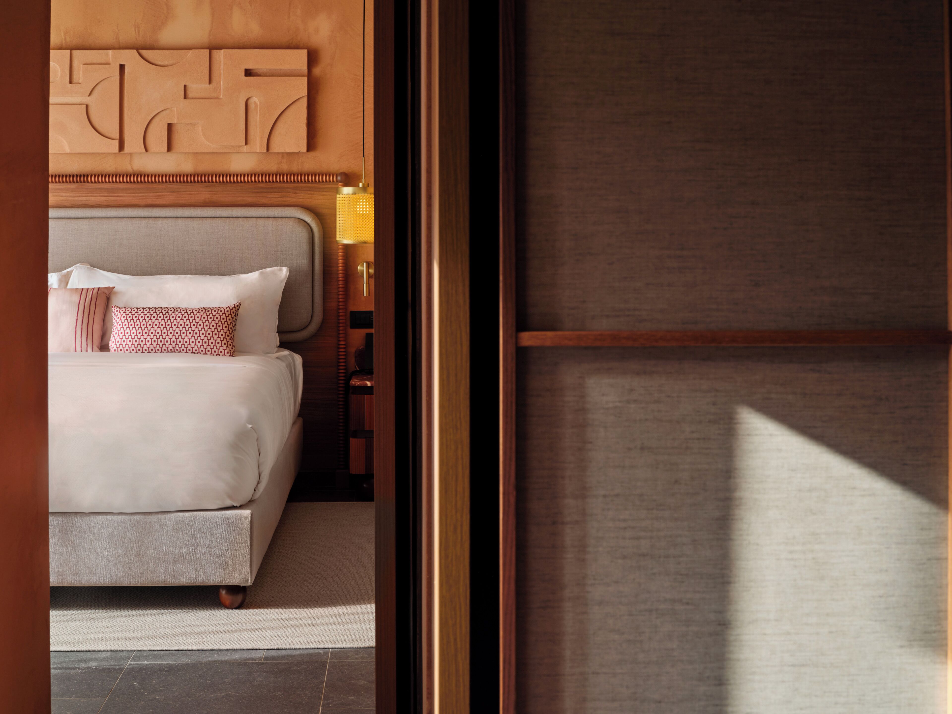 A hotel room with a bed, a nightstand, and a wall-mounted light fixture.