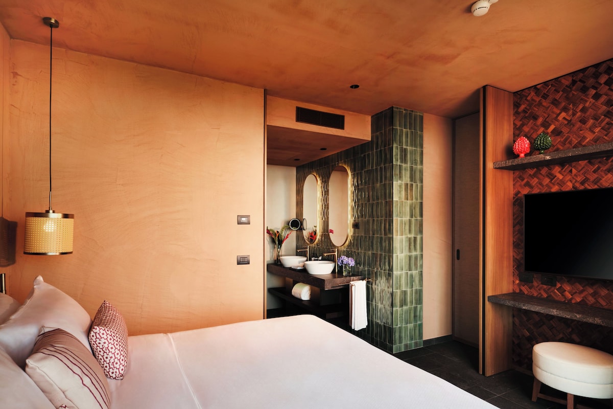 A hotel room with a large bed, a bathroom with a mirror and sink, and a TV mounted on the wall.