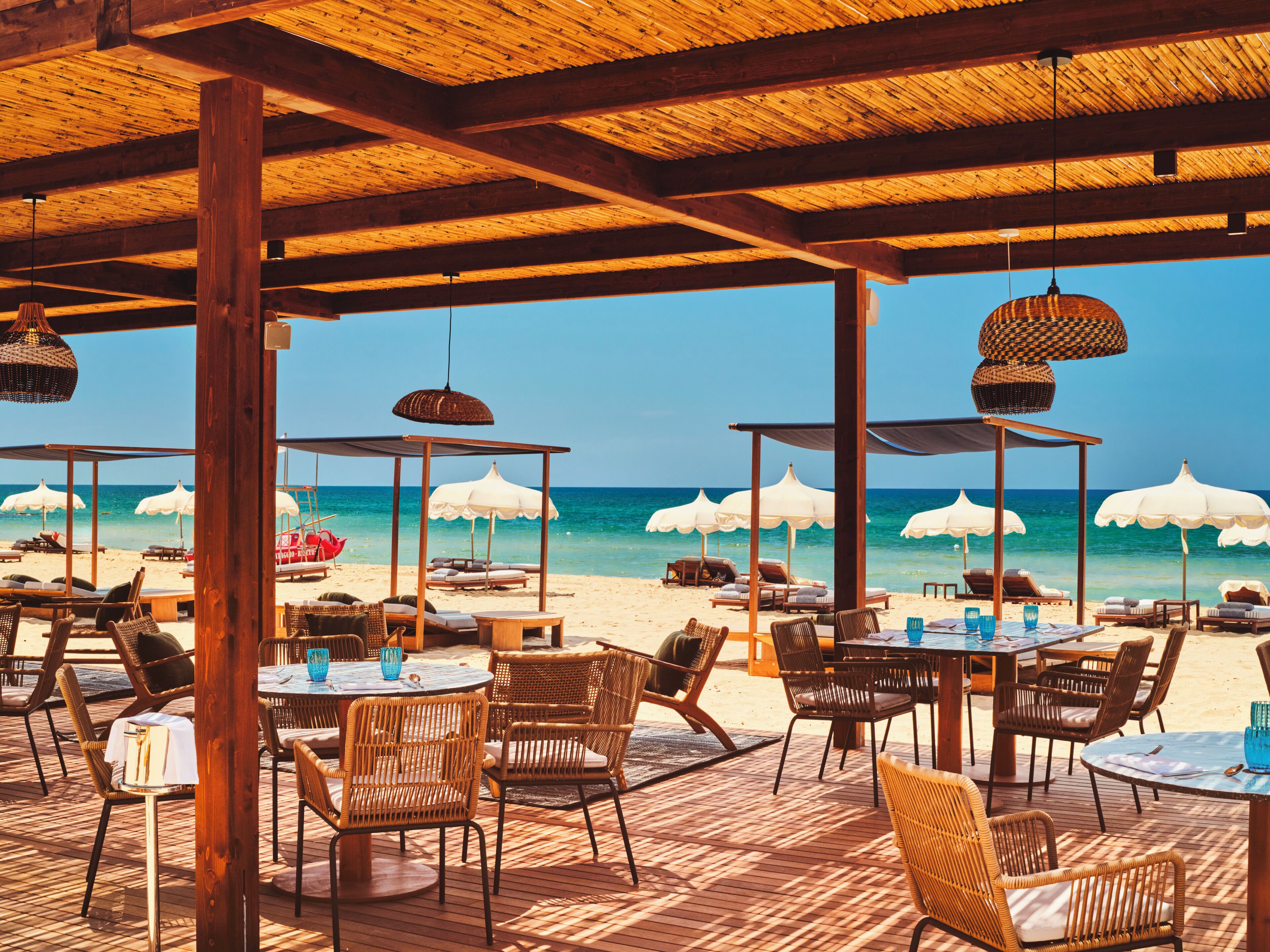 Un ristorante sulla spiaggia con posti a sedere all'aperto, ombrelloni e vista sull'oceano.