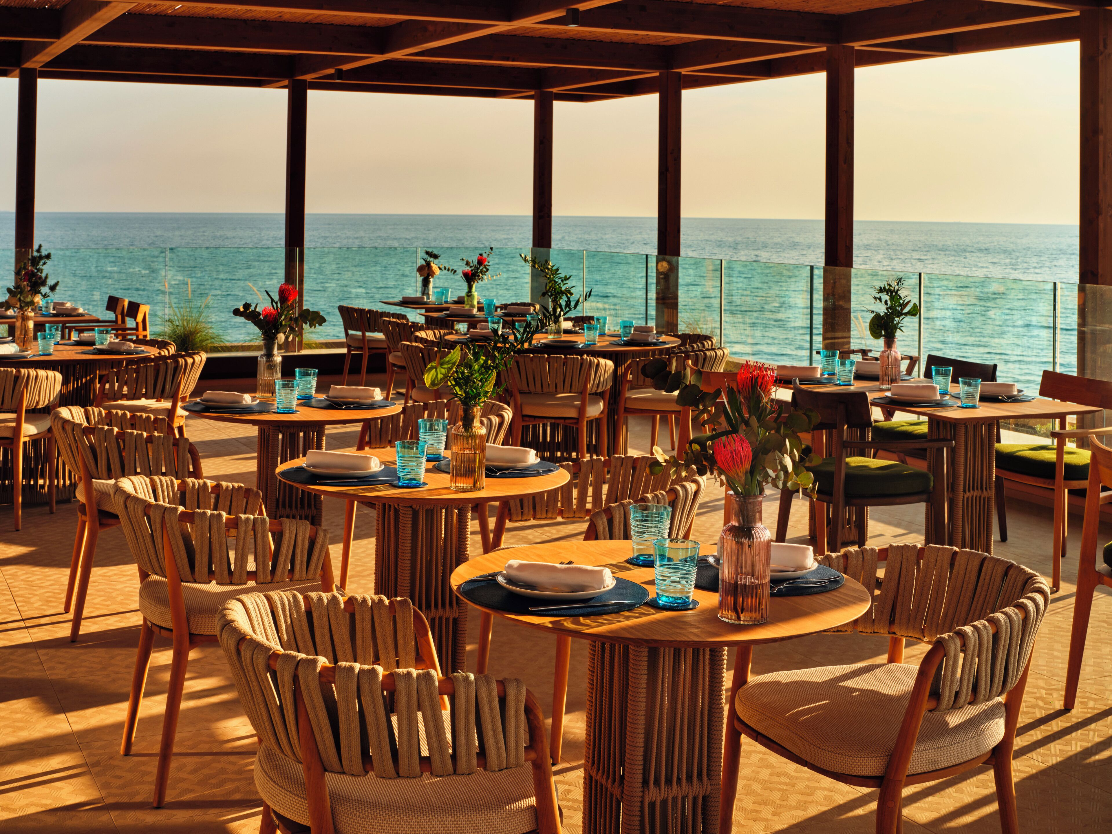 An outdoor dining area with tables and chairs, overlooking the sea.