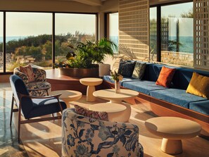 A modern living room with a sofa, chairs, and a coffee table, overlooking a scenic view. -  Icona's Costa Ragusa Resort (Scoglitti)