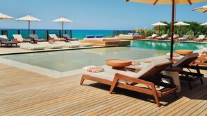A poolside area with lounge chairs and umbrellas, a wooden deck, and a view of the ocean. -  Icona's Costa Ragusa Resort - New Opening (Scoglitti)