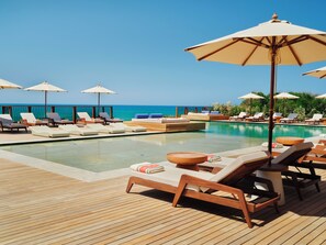 Un área junto a la piscina con sillones de descanso y sombrillas, una terraza de madera y vistas al océano.
