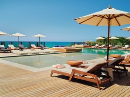 Un área junto a la piscina con sillones de descanso y sombrillas, una terraza de madera y vistas al océano.
