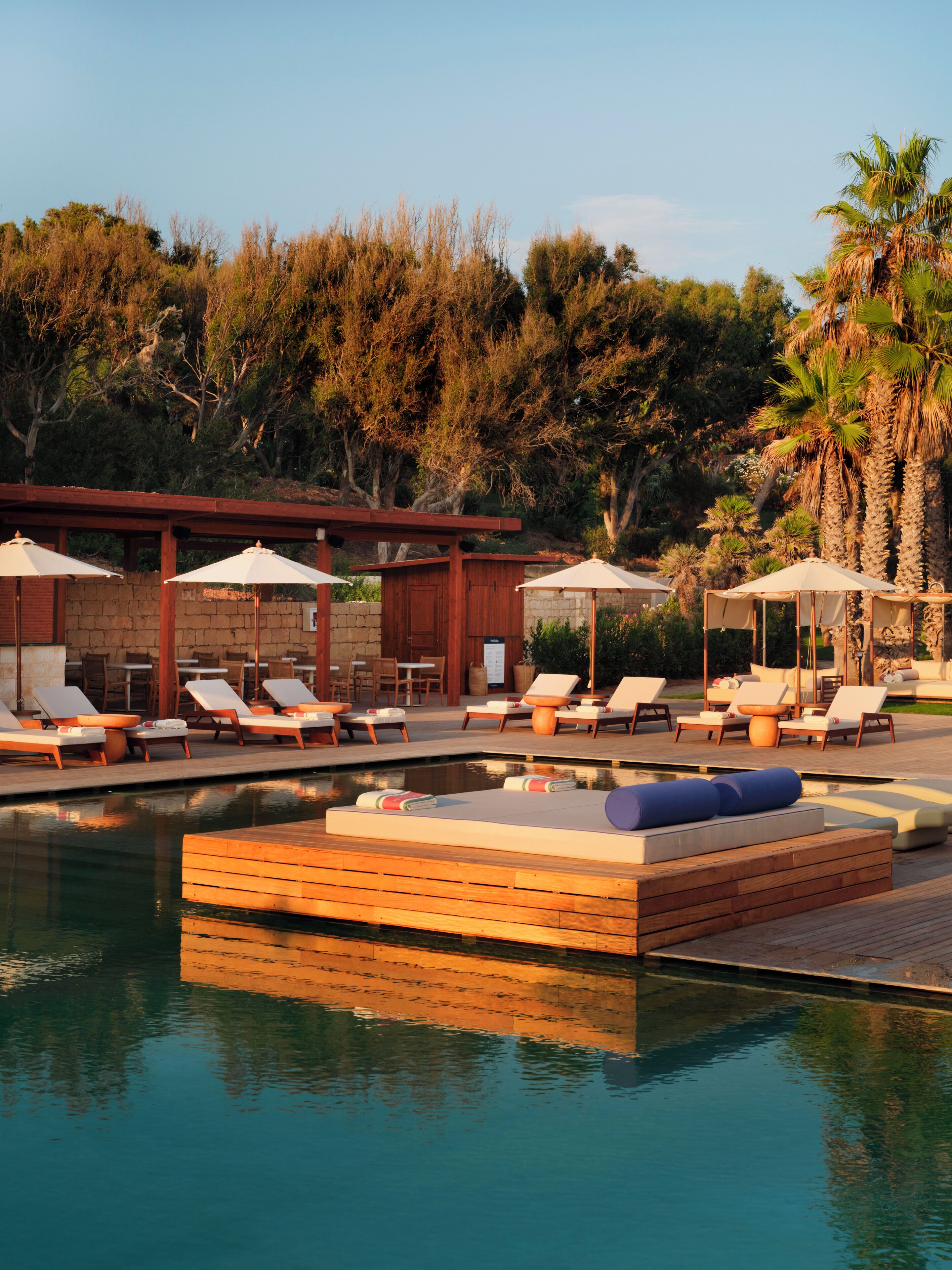 Zona junto a la piscina con sillas de descanso, sombrillas y una terraza de madera.