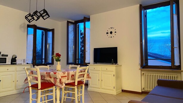 Une cuisine moderne avec une table à manger, des chaises, un téléviseur et de grandes fenêtres donnant sur l’extérieur.