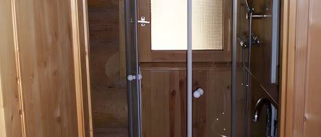 A wooden cabin bathroom with a shower enclosure, a sink, and a window.