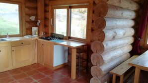 A log cabin with a kitchen area, including a stove, sink, and window. - Le chalet neige – Chorges Hautes-Alpes (Chorges)