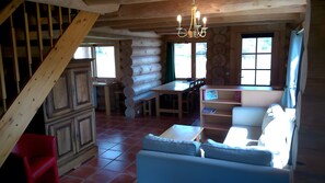 L’intérieur d’une cabane en rondins, avec un coin repas, un canapé et un escalier.