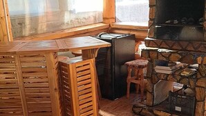 A rustic kitchen with a stone fireplace, wooden furniture, and a large window. - Enchanting 2-bedroom house with AC and Barbecue in charming Mălaia (Mălaia)