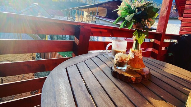 A wooden deck with a table, a white mug, and a floral arrangement. - Enchanting 2-bedroom house with AC and Barbecue in charming Mălaia (Mălaia)