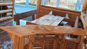 A wooden outdoor seating area with a table and stools, surrounded by a wooden fence and a view of trees. - Enchanting 2-bedroom house with AC and Barbecue in charming Mălaia (Mălaia)