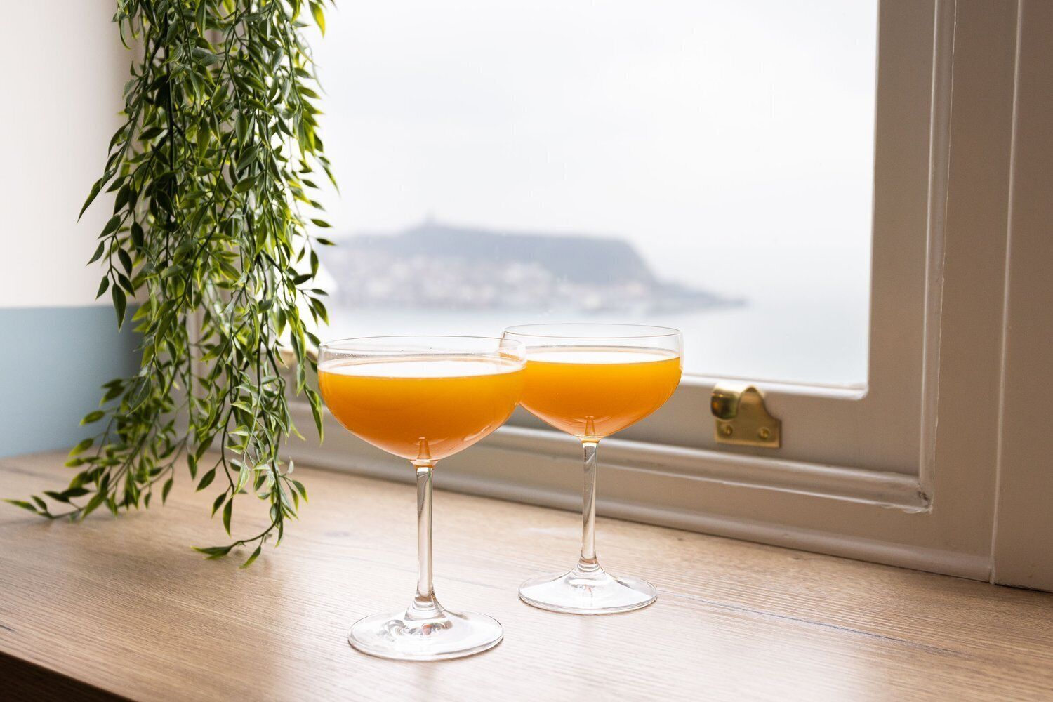 Dois copos de suco de laranja em um parapeito de janela com vista para a paisagem urbana.