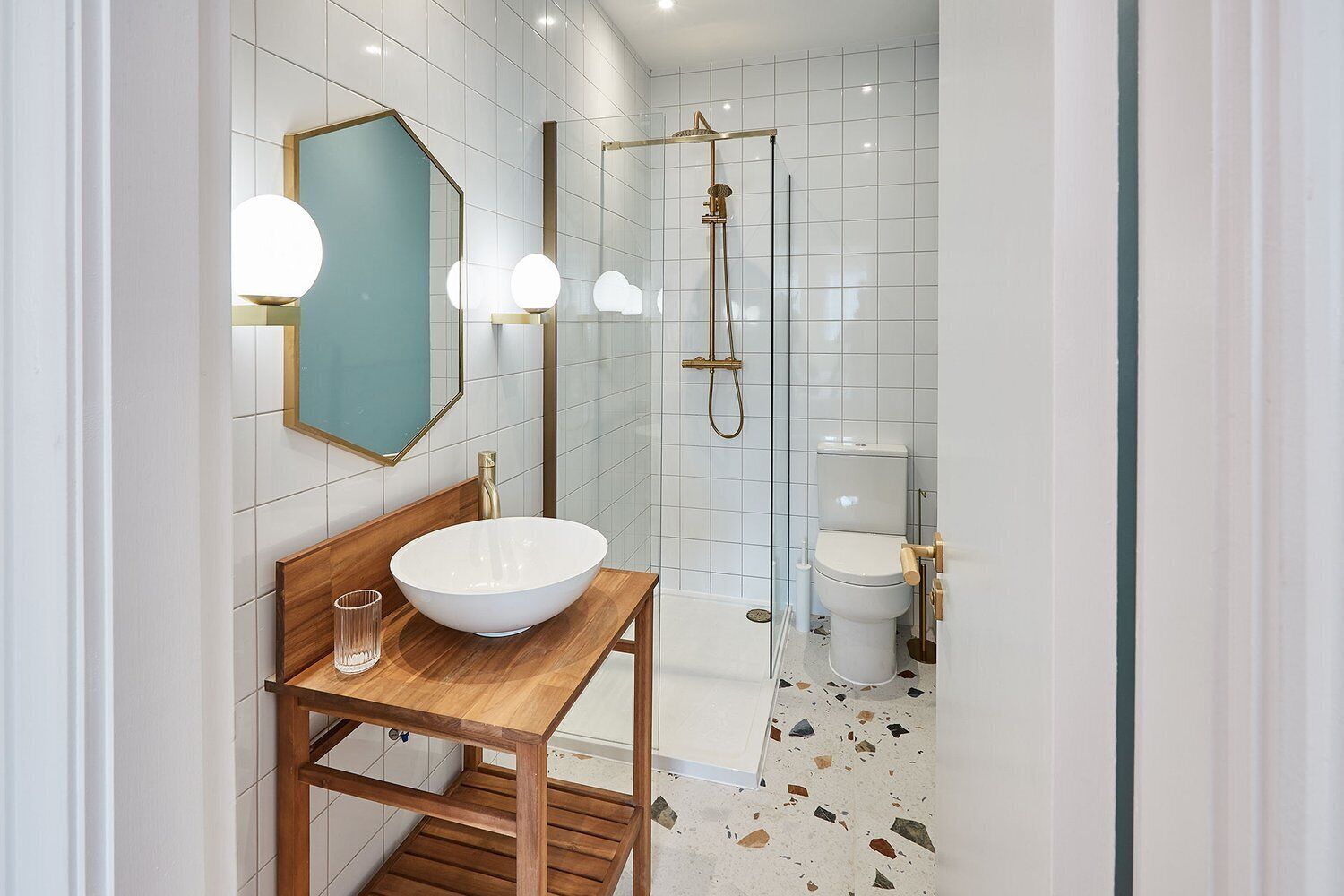 A modern bathroom with a wooden vanity, a large white basin, a glass shower enclosure, and a toilet.