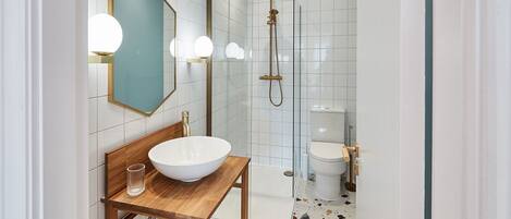 A modern bathroom with a wooden vanity, a large white basin, a glass shower enclosure, and a toilet.