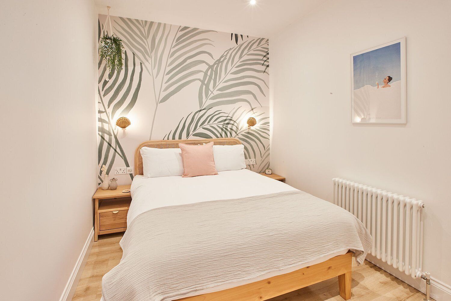 A bedroom with a bed, bedside lamps, a nightstand, a wall-mounted radiator, and a framed picture on the wall.