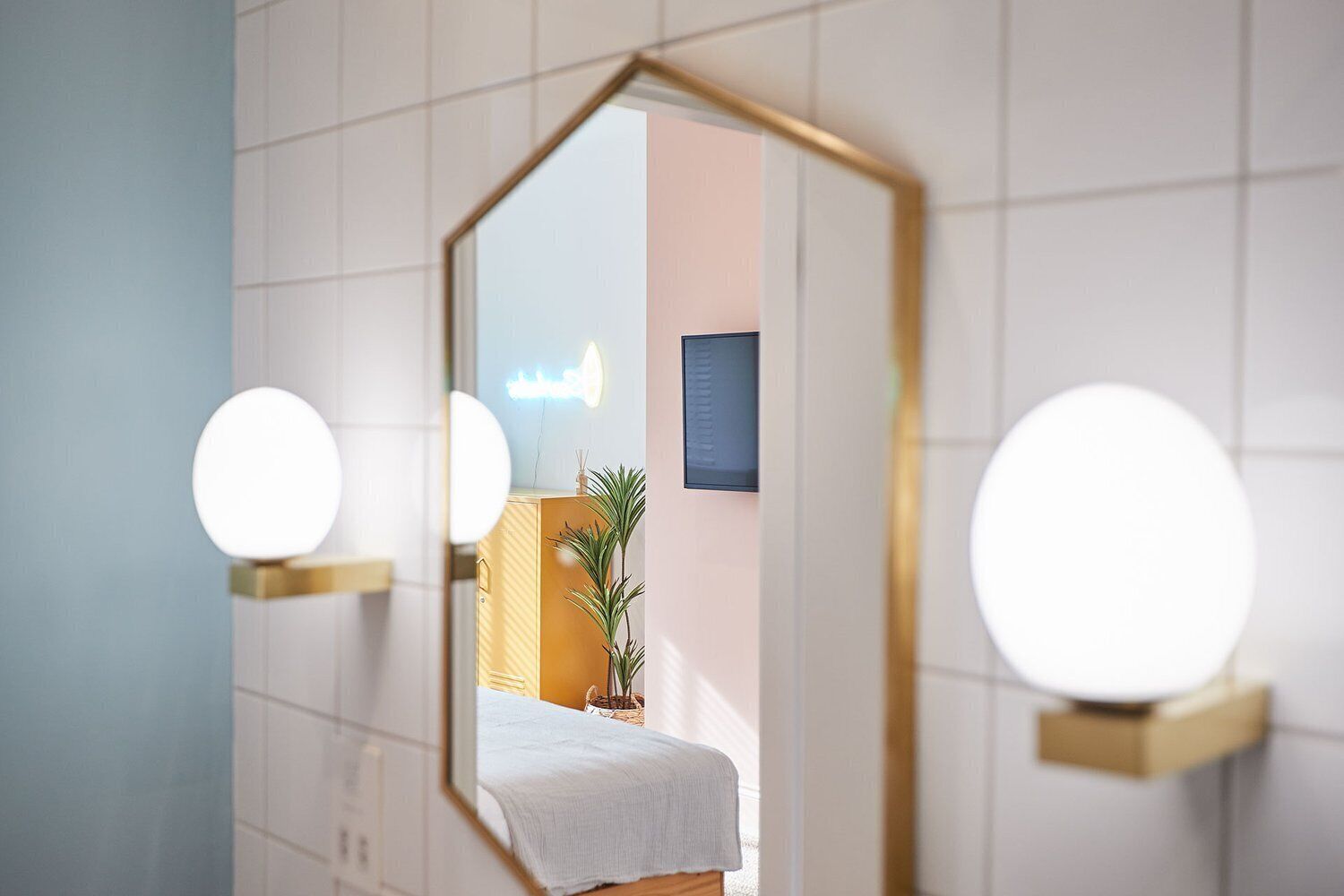 Une salle de bain dotée d’un grand miroir, d’appliques murales rondes et d’un lit visible, agrémenté d’une plante.