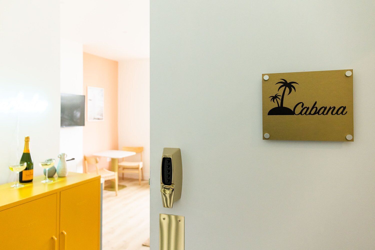 Habitación de hotel con una nevera minibar amarilla, un lector de llavecard montado en la pared y un cartel que dice 'Cabana'.