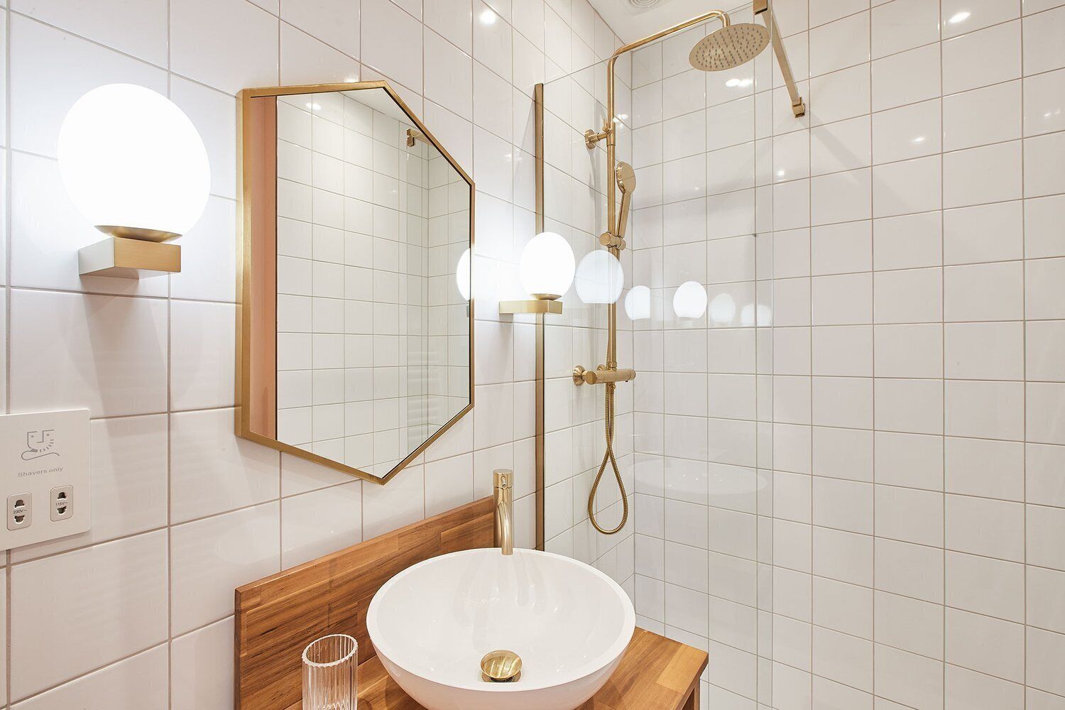A modern bathroom with a white sink, a large mirror, and a gold shower system.